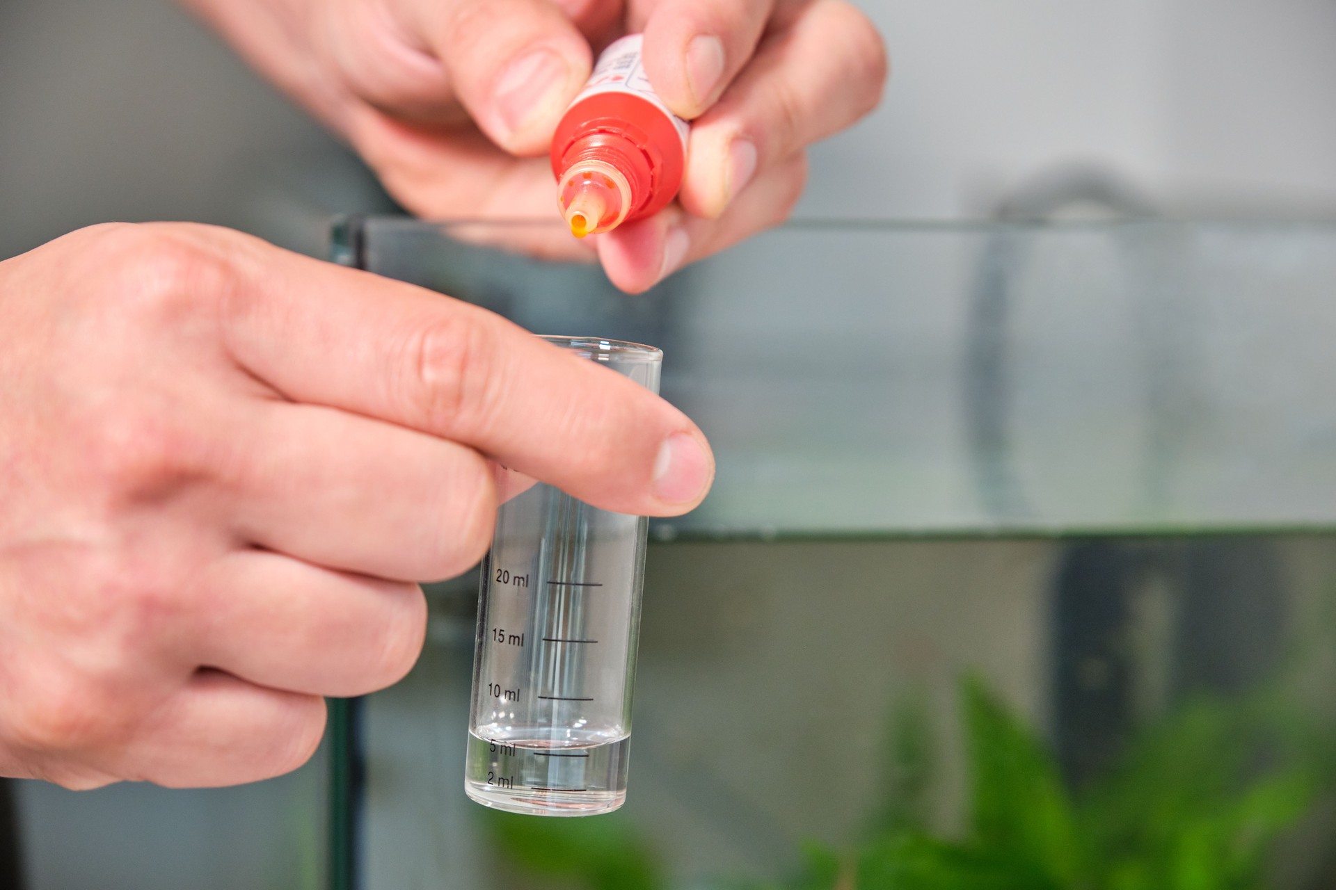 Hands adding drops to test PH or nitrite in front of freshwater aquarium.